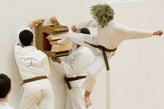 A brown belt breaks five boards with a head-high jumping side kick.
